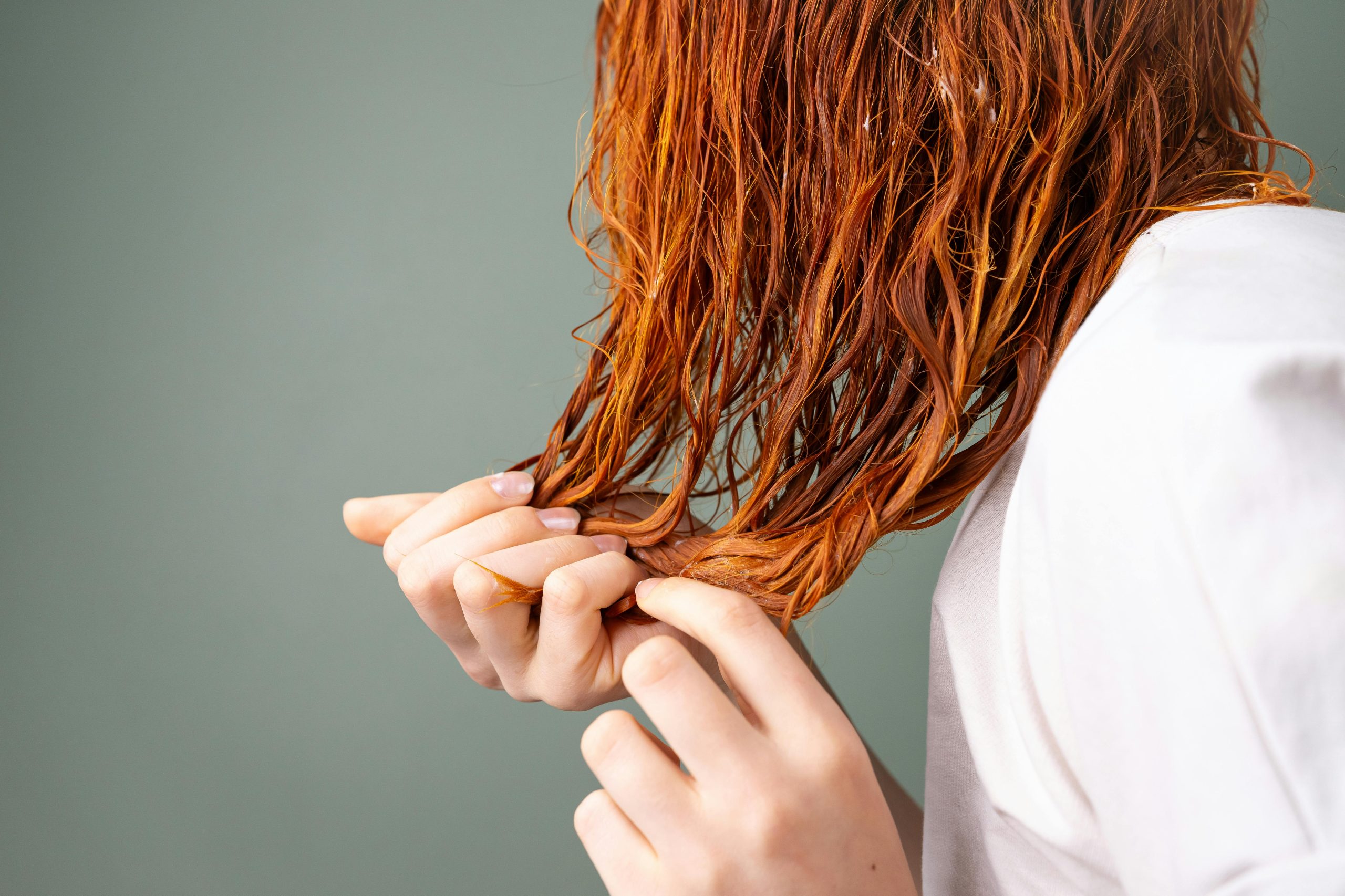 A detailed image showing a close-up of red hair being held by delicate hands against a neutral background.