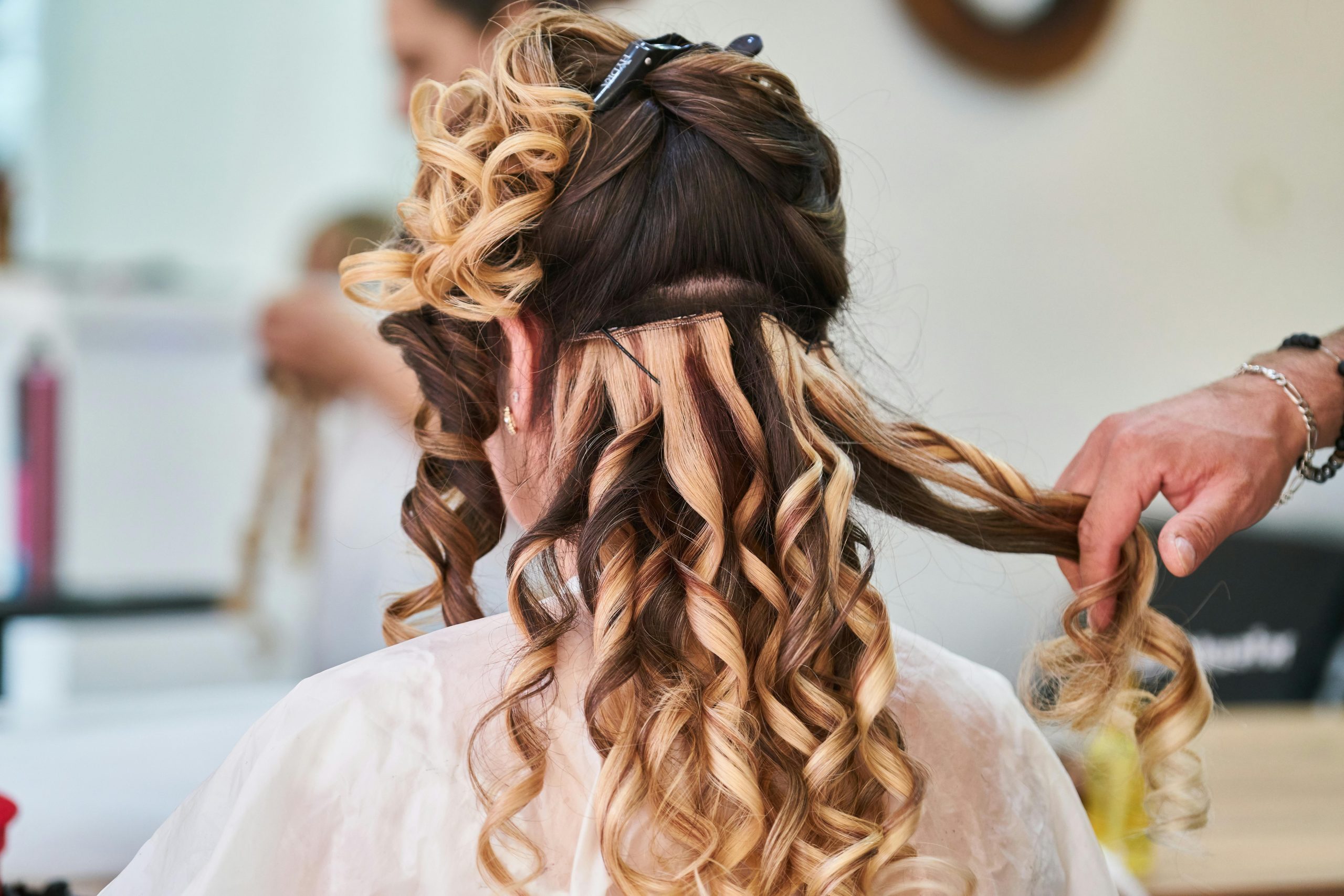 Close-up of hairstylist perfecting curls on a woman's hair in a salon setting.