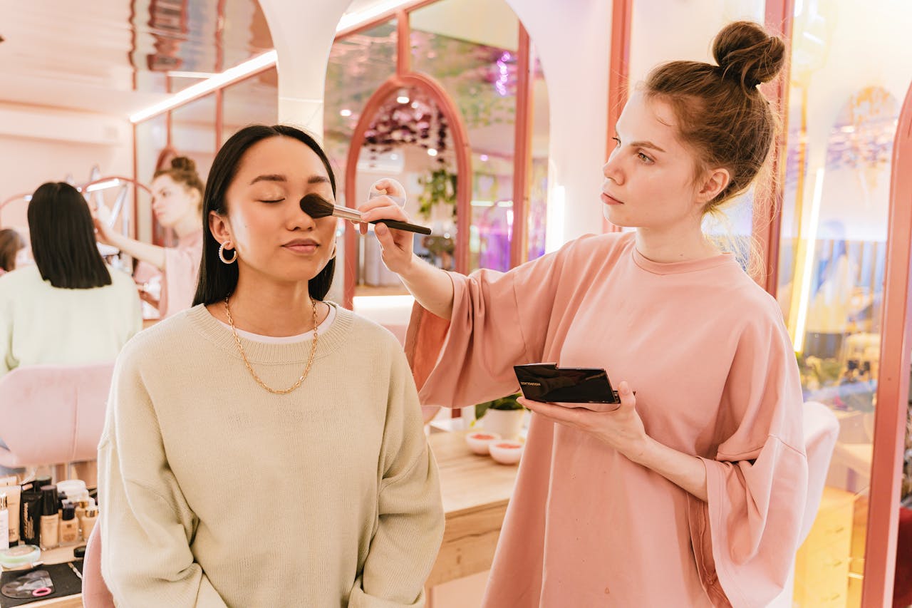 Woman in Peachy Oversize T-Shirt Doing Makeup to Woman with Closed Eyes