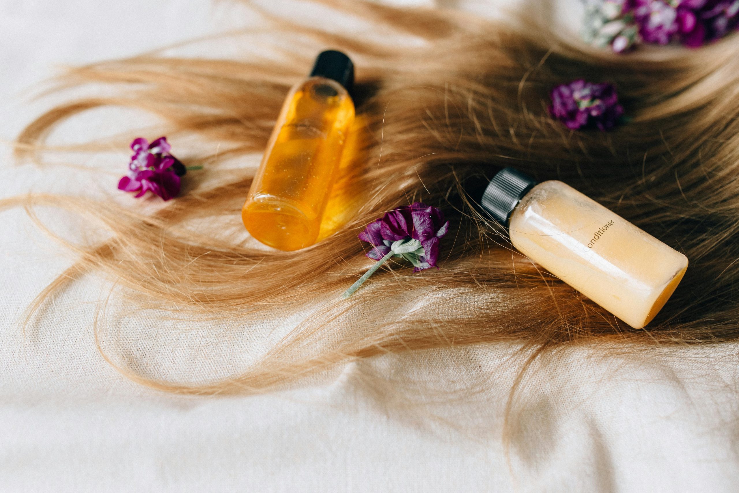 Hair care products on a bed of hair and flowers, symbolizing luxury and beauty.