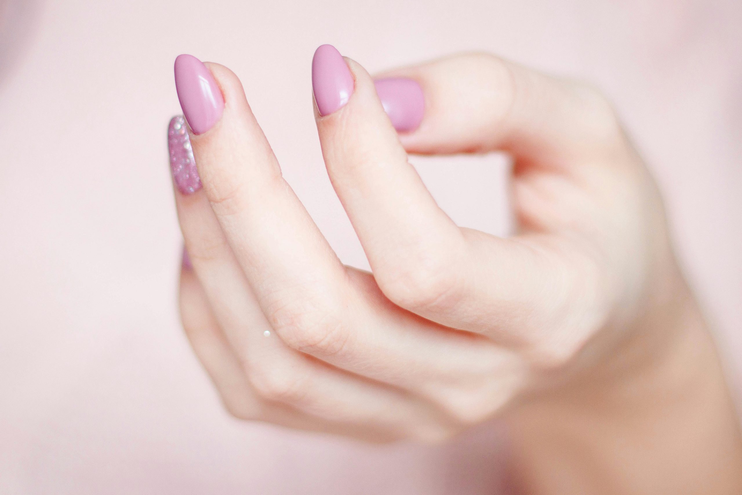 A close-up of a woman's hand showing a stylish pink and glittery manicure.