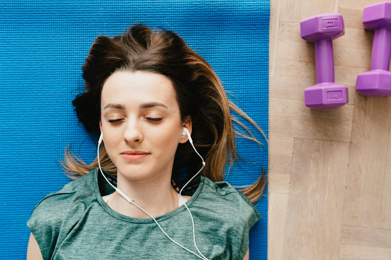 A young woman lying on a mat with earphones, relaxing in a peaceful indoor setting.