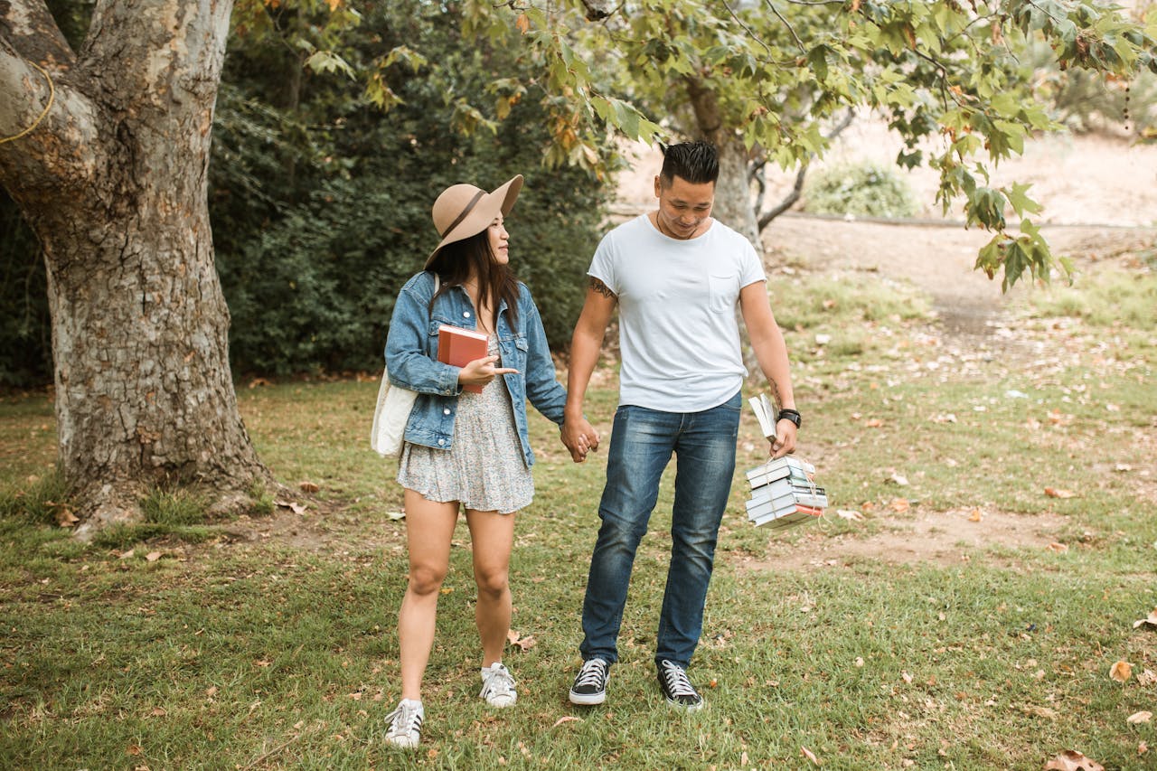 Happy couple holding hands and enjoying a walk in a sunny park, carrying books.