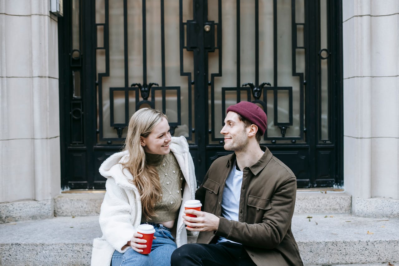 A happy couple sharing a coffee moment on a city staircase, enjoying their time together.