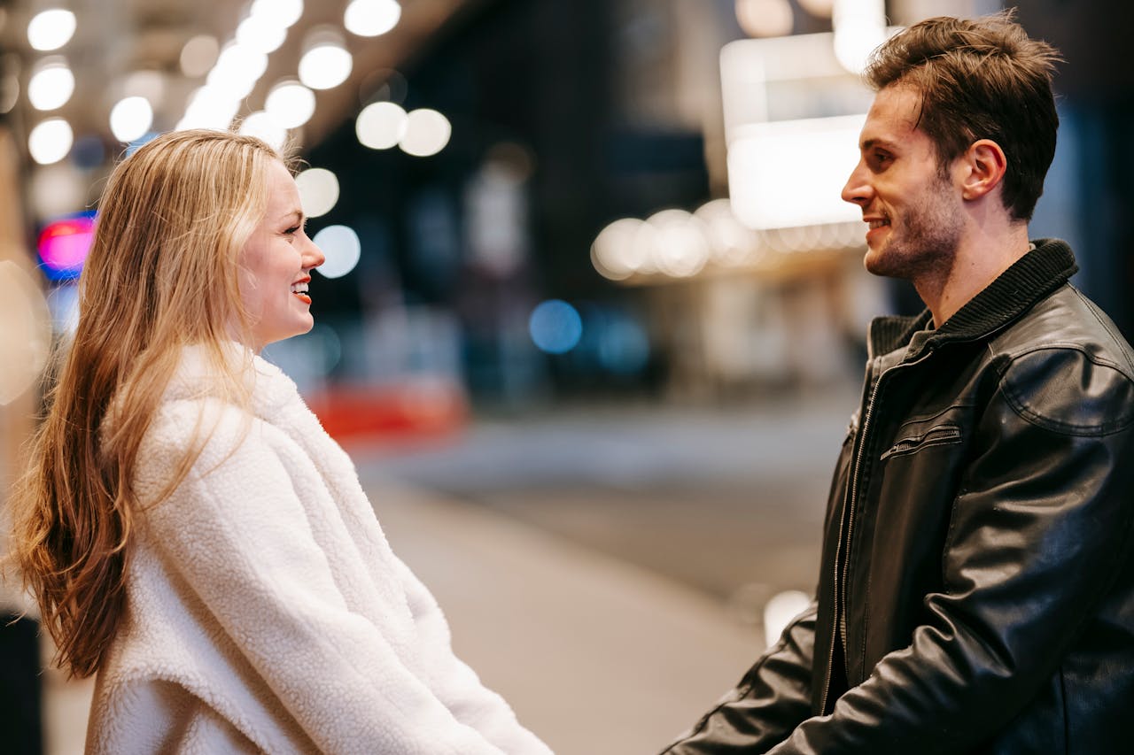 A couple shares a romantic moment holding hands with bokeh lights at night.